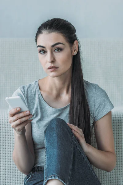 Triste giovane donna in possesso di smartphone e guardando la fotocamera — Foto stock