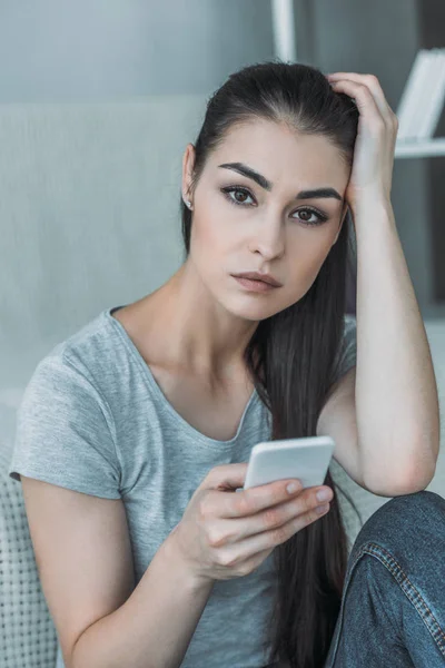 Verärgerte junge Frau hält Smartphone in der Hand und blickt in Kamera — Stockfoto