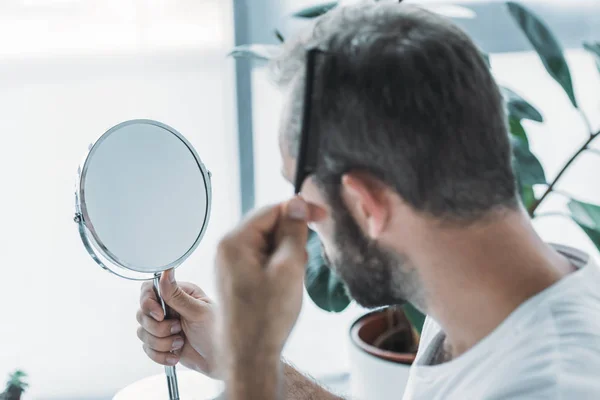 Чоловік середнього віку розчісує волосся і дивиться на дзеркало, концепція втрати волосся — стокове фото