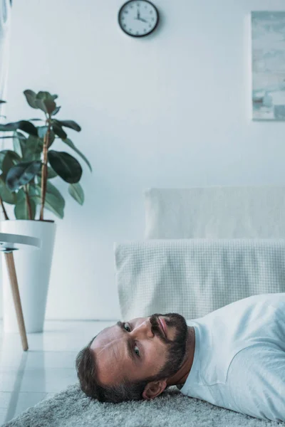 Depressive bearded middle aged man lying on carpet and looking at camera — Stock Photo