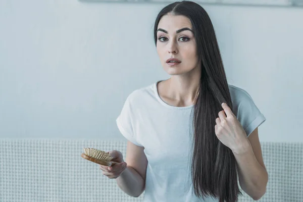 Upset brunette woman holding hairbrush and looking at camera, hair loss concept — Stock Photo