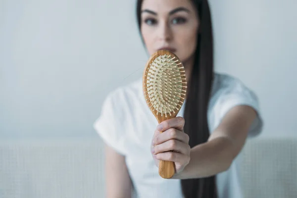 Close-up view of young woman holding hairbrush with fallen hair on grey — Stock Photo