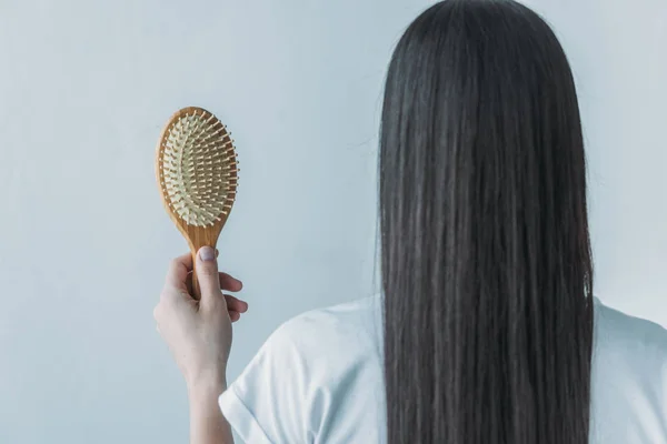 Visão traseira da mulher morena segurando escova de cabelo com cabelo caído isolado no cinza — Fotografia de Stock