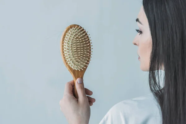 Plan recadré de femme brune tenant une brosse à cheveux avec des cheveux tombés isolés sur gris — Photo de stock