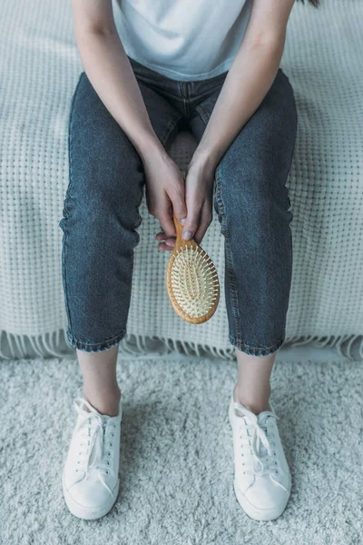 Abgeschnittene Aufnahme einer jungen Frau, die eine Bürste hält und auf einer Couch sitzt, Haarausfall-Konzept — Stockfoto