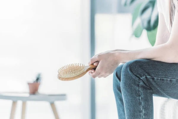 Cropped shot of young woman holding hairbrush while sitting indoors, hair loss concept — Stock Photo