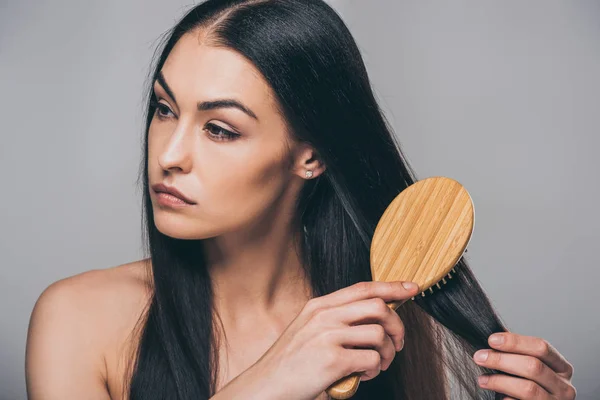 Frustrata bruna ragazza pettinando i capelli e distogliendo lo sguardo isolato sul grigio — Foto stock