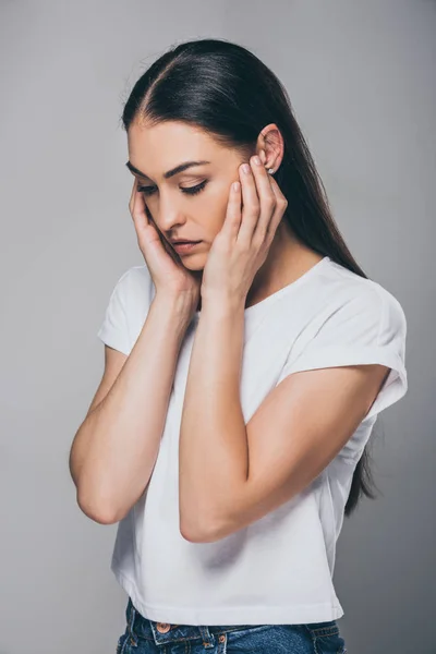 Traurige brünette Frau mit den Händen im Gesicht, die isoliert auf grau herabblickt — Stockfoto