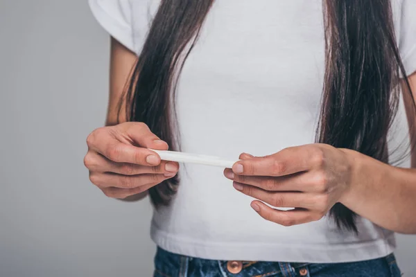 Plan recadré de jeune femme brune tenant un test de grossesse isolé sur gris — Photo de stock