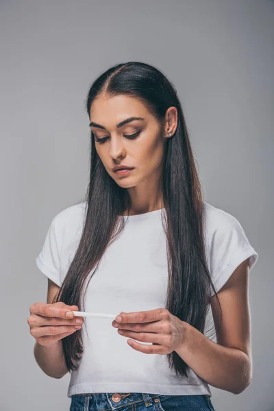 Mujer joven disgustada sosteniendo prueba de embarazo aislada en gris - foto de stock