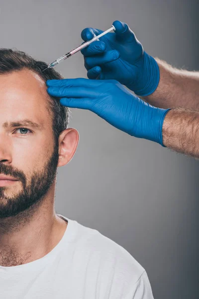 Tiro recortado do doutor com seringa que dá a injeção ao homem com alopecia que olha para a câmera isolada no cinza — Fotografia de Stock