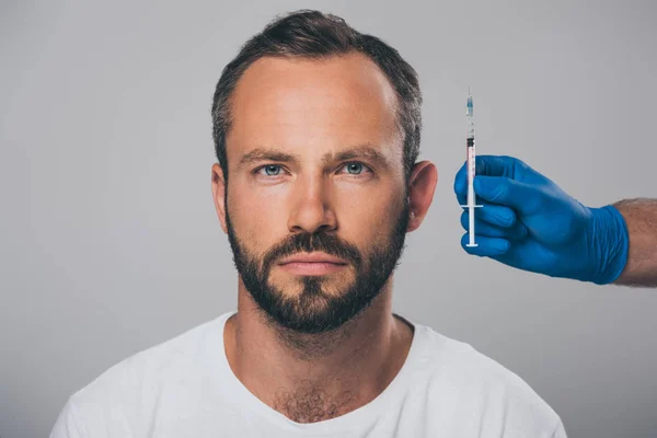 Médecin tenant la seringue dans la main et l'homme avec alopécie regardant la caméra isolée sur gris — Photo de stock