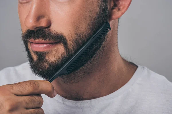 Cropped shot of bearded man combing beard with comb isolated on grey — Stock Photo