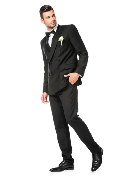 Novio joven sonriente en traje elegante con boutonniere mirando hacia atrás aislado en blanco - foto de stock