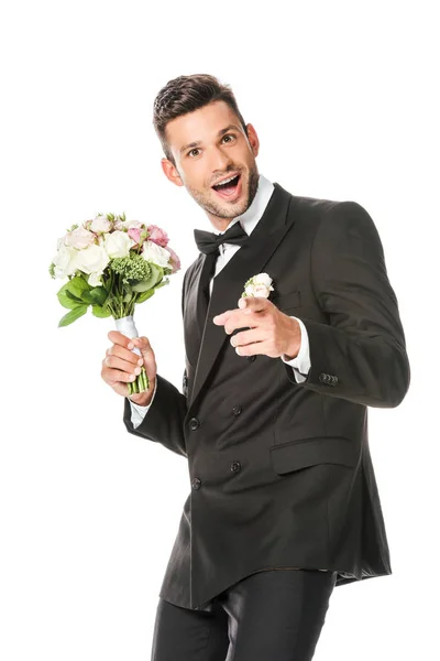 Happy young groom with bridal bouquet pointing at camera isolated on white — Stock Photo