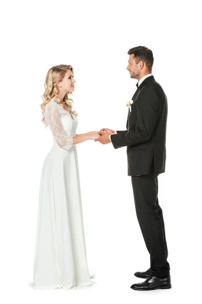 Happy young bride and groom holding hands and looking at each other isolated on white — Stock Photo