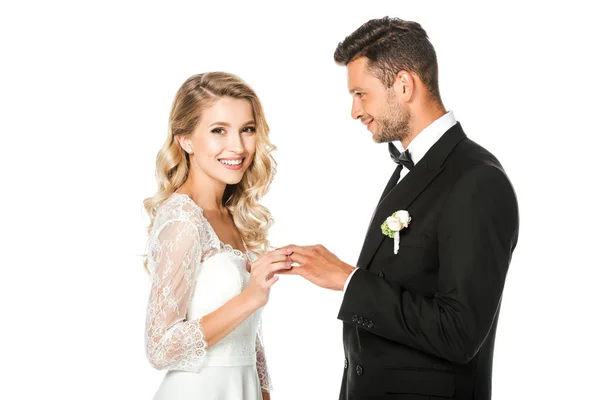 Happy young bride putting on wedding ring on grooms finger isolated on white — Stock Photo