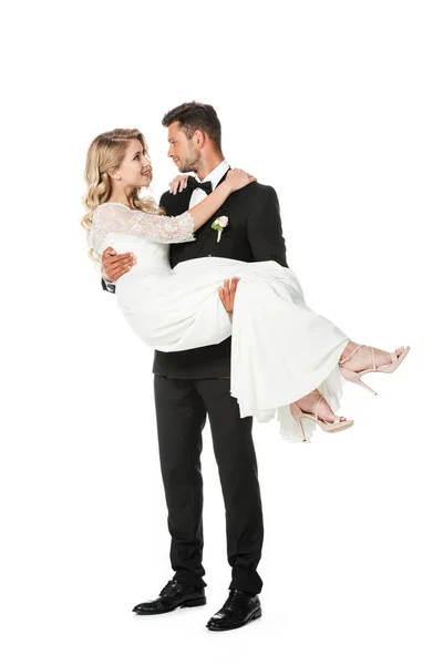 Smiling young groom carrying his bride isolated on white — Stock Photo