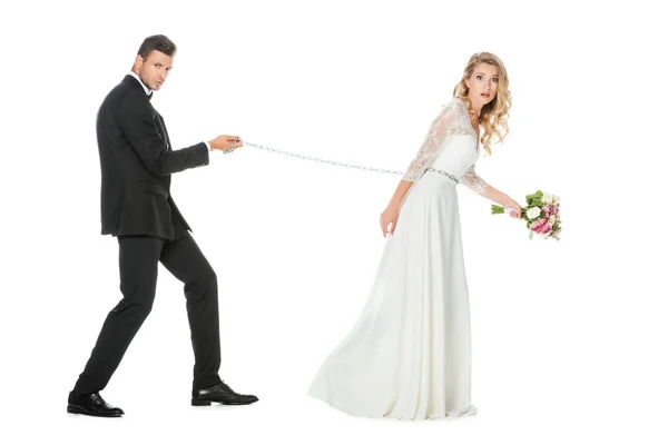 Vista laterale di giovane sposo con catena e guinzaglio scioccato sposa isolato su bianco — Foto stock