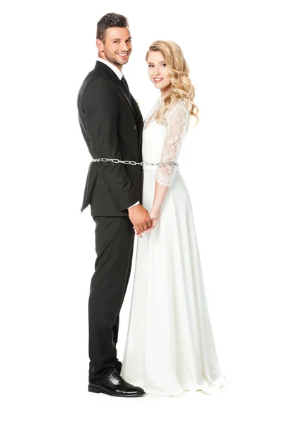 Happy young newlyweds tied with chain back to back and looking at camera isolated on white — Stock Photo