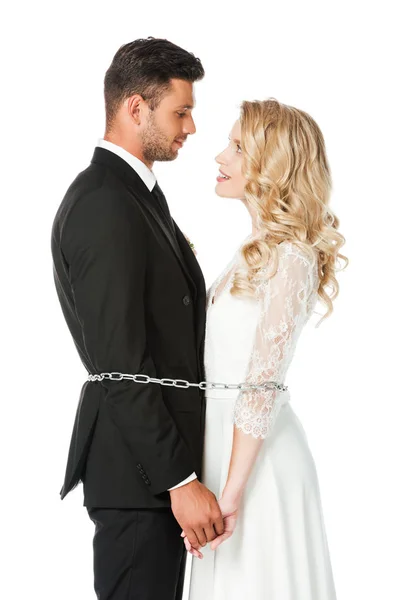 Beautiful young newlyweds tied with chain and looking at each other  isolated on white — Stock Photo