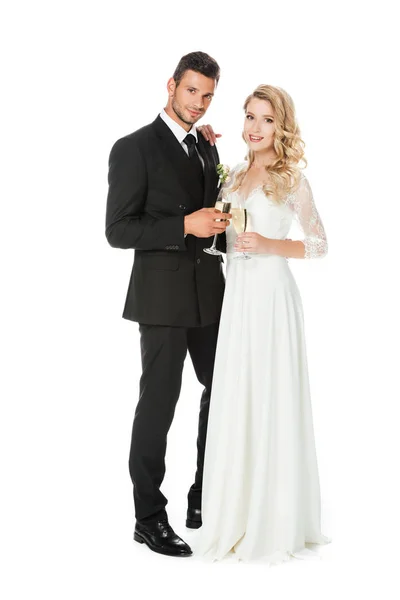 Happy young bride and groom with glasses of champagne looking at camera isolated on white — Stock Photo