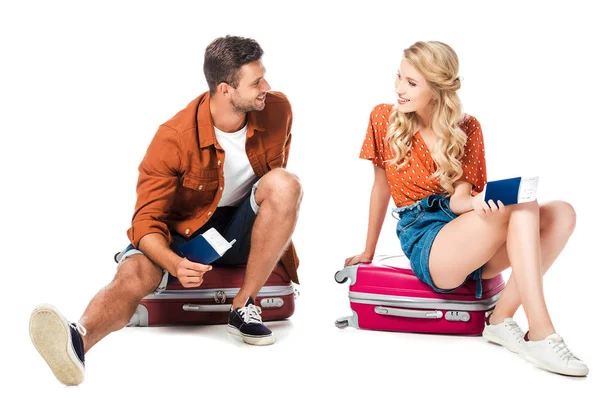 Smiling couple sitting on travel bags with passports and tickets isolated on white — Stock Photo