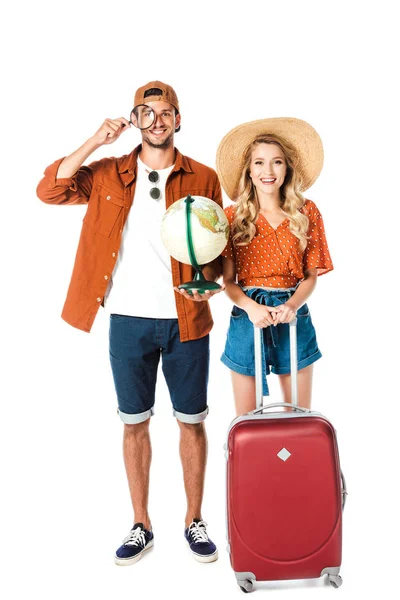 Sonriente pareja de pie con lupa, globo y bolsa de viaje aislados en blanco - foto de stock