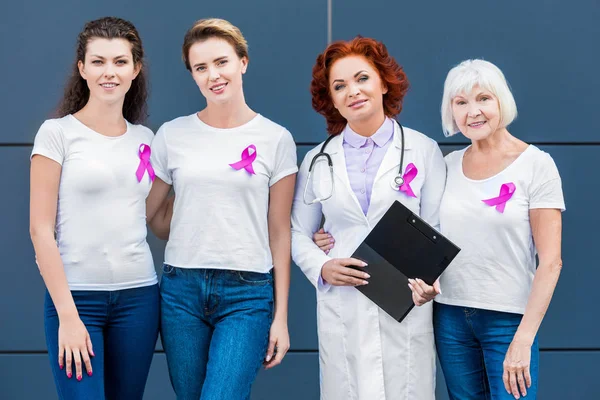 Women and doctor with pink ribbons standing together and smiling at camera, breast cancer awareness concept — Stock Photo