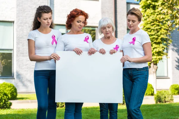 Les femmes avec des rubans de sensibilisation au cancer du sein tenant une bannière vierge et regardant vers le bas — Photo de stock