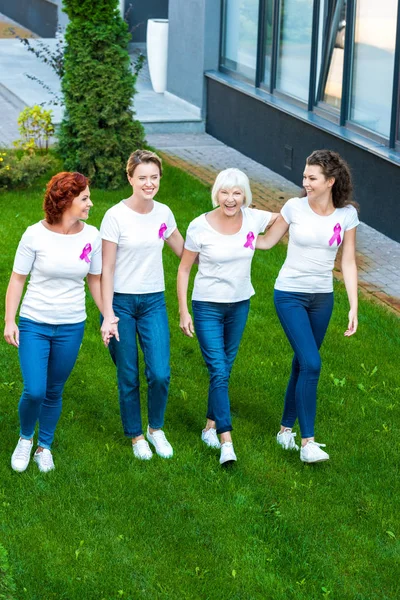 Vue grand angle de quatre femmes souriantes avec des rubans de sensibilisation au cancer du sein marchant ensemble — Photo de stock