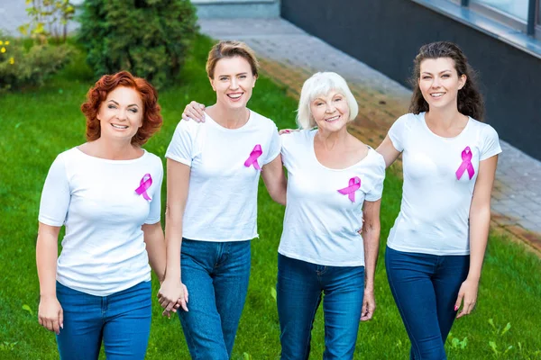Высокий угол обзора четырех женщин с лентами для информирования о раке молочной железы, держащихся за руки и улыбающихся в камеру — стоковое фото