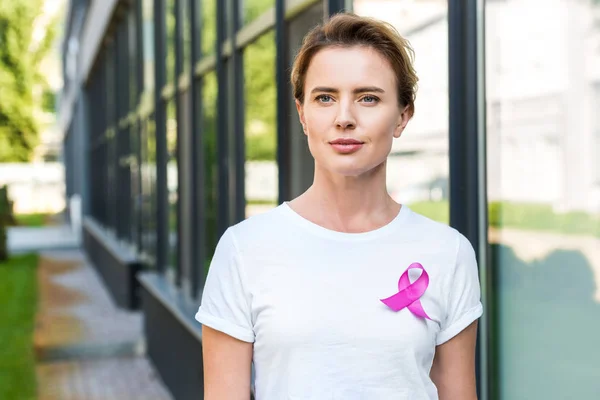 Pensive middle aged woman with pink ribbon standing on street, breast cancer awareness concept — Stock Photo