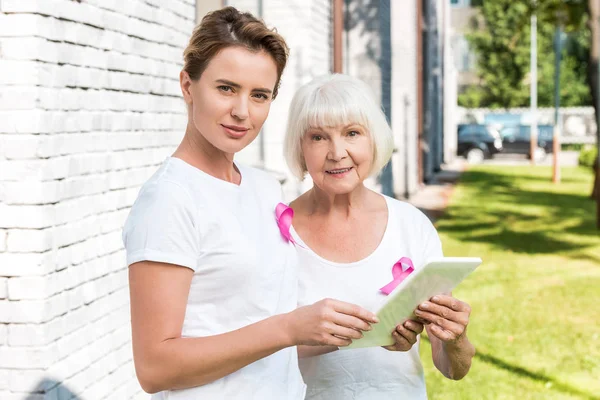 Frauen mit Brustkrebs-Sensibilisierungsbändern nutzen digitales Tablet und lächeln in die Kamera — Stockfoto