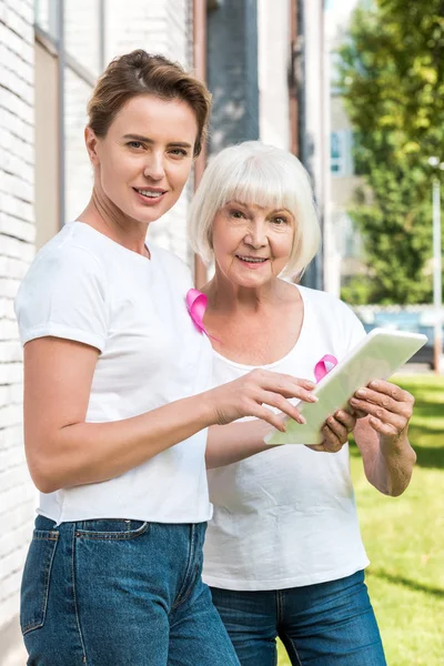 Женщин, использующих цифровой планшет и улыбающихся в камеру, концепция информированности о раке груди — стоковое фото