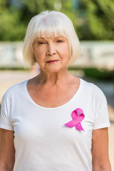 Mulher sênior com fita rosa olhando para câmera, conceito de consciência de câncer de mama — Fotografia de Stock