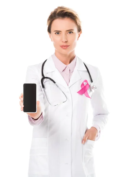 Doctor with pink ribbon holding smartphone with blank screen and looking at camera isolated on white, breast cancer awareness concept — Stock Photo