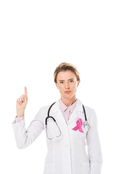 Doctor with pink ribbon pointing up with finger and looking at camera isolated on white, breast cancer awareness concept — Stock Photo