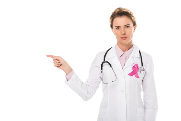 Doctor with pink ribbon pointing with finger and looking at camera isolated on white, breast cancer awareness concept — Stock Photo