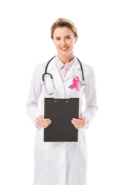 Doctor with pink ribbon holding clipboard and smiling at camera isolated on white, breast cancer awareness concept — Stock Photo