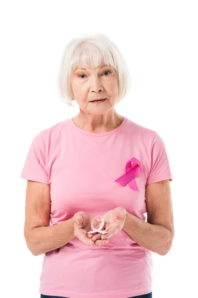 Donna anziana che tiene il nastro rosa e guarda la fotocamera isolata sul bianco, concetto di cancro al seno — Foto stock
