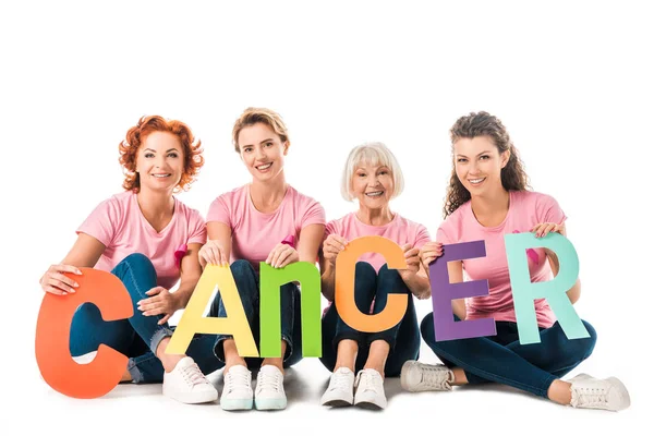 Women in pink t-shirts holding colorful letters with word cancer and smiling at camera isolated on white — Stock Photo