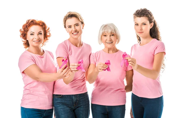 Женщины в розовых футболках, держащие ленты для информирования о раке груди и улыбающиеся в камеру, изолированную на белом — стоковое фото