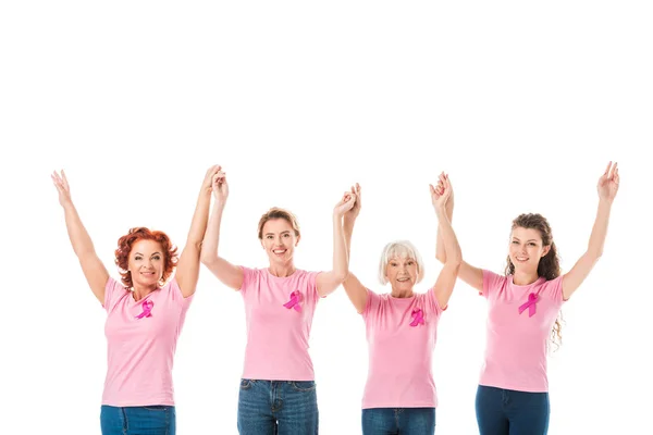 Mulheres em camisetas rosa com fitas de consciência de câncer de mama de mãos dadas e sorrindo para a câmera isolada em branco — Fotografia de Stock