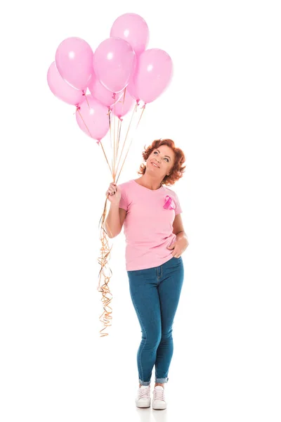 Mujer sonriente sosteniendo racimo de globos rosados y mirando hacia arriba aislado en blanco, concepto de cáncer de mama - foto de stock
