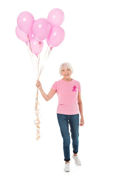 Femme âgée souriante tenant des ballons roses et regardant la caméra isolée sur blanc, concept de sensibilisation au cancer du sein — Photo de stock