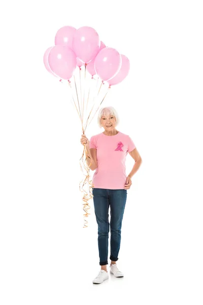 Full length of senior woman holding pink balloons and smiling at camera isolated on white, breast cancer awareness concept — Stock Photo