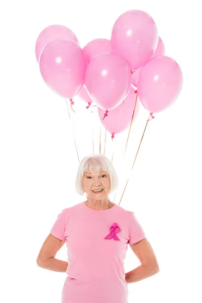 Senior woman holding pink balloons and smiling at camera isolated on white, breast cancer awareness concept — Stock Photo