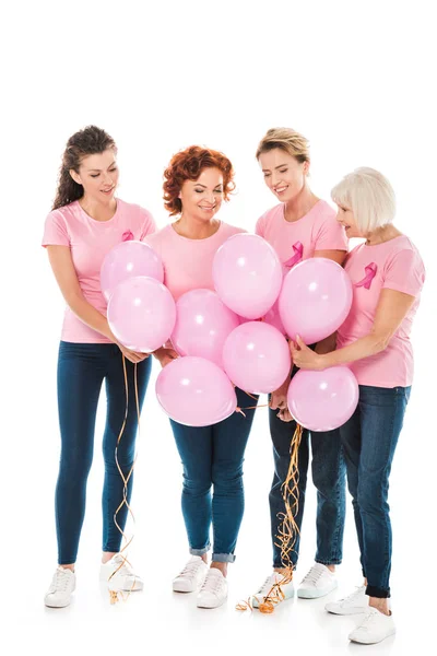 Mujeres sonrientes con cintas de conciencia de cáncer de mama sosteniendo racimo de globos rosados aislados en blanco - foto de stock