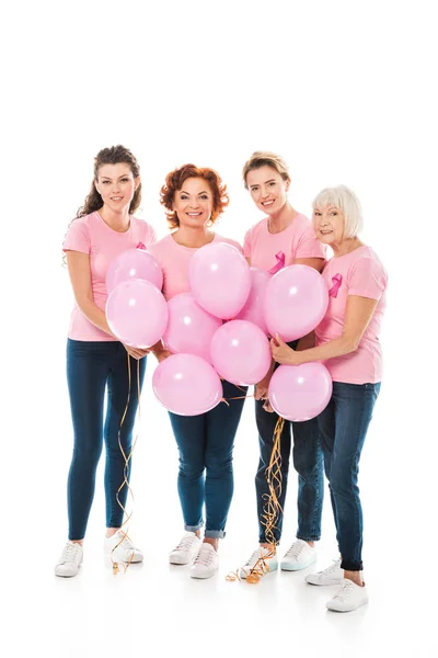Mujeres con cintas de conciencia de cáncer de mama sosteniendo racimo de globos rosados y sonriendo a la cámara aislada en blanco - foto de stock